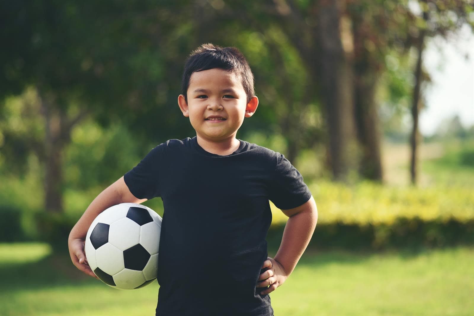 Niño sonriente sostiene un balón de fútbol al aire libre