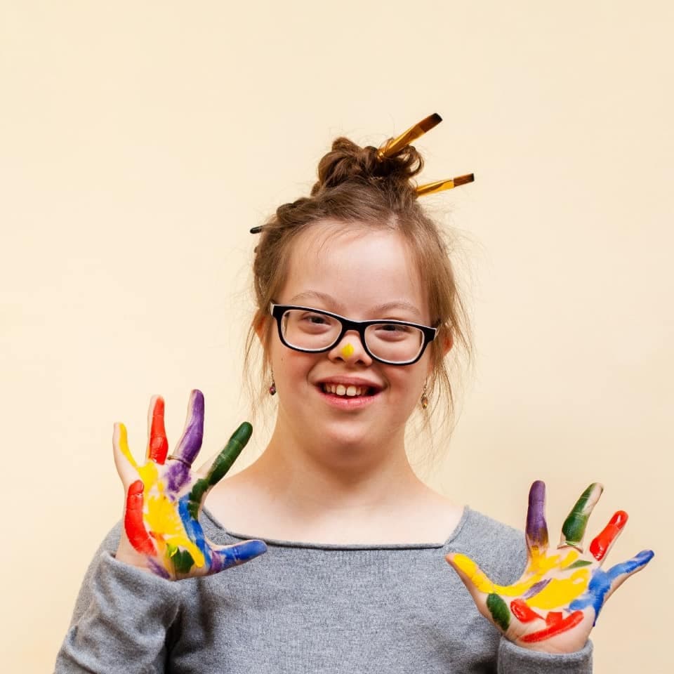Niña sonriente muestra las palmas de sus manos pintadas de colores